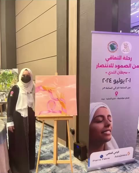 إحدى مبدعات ناجية بجانب لوحتها المعروضة في الملتقى.